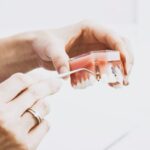 A close-up of hands holding a dental model while using a tool to demonstrate a dental implant.